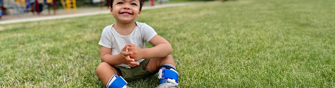 Toddler with orthotics on legs sitting in the grass for orthotic videos page